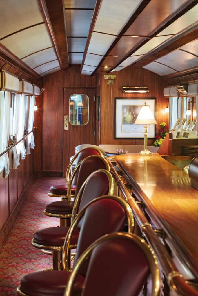 Elegant train interior featuring a wooden bar and large seats with brass details offering a view of the large interior train cabin.