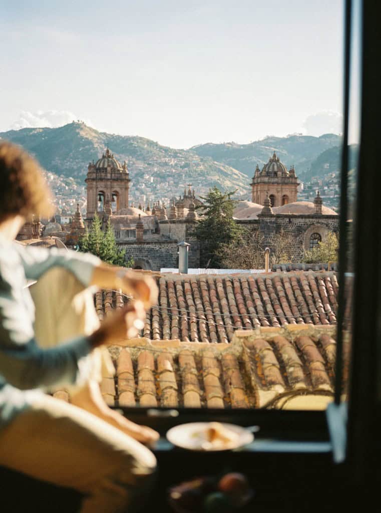 Woman enjoying a snack while sittig on a windowsill at a hotel and looking out to the architectural beautiful scenery of Peru 