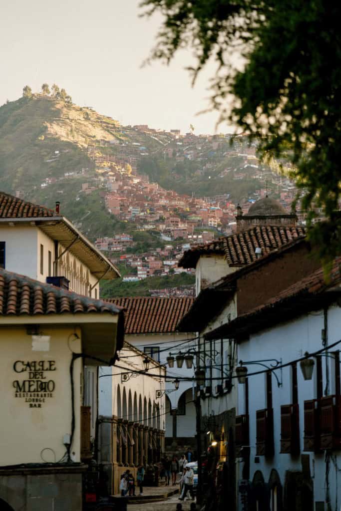 Scenic view of a historic Peruvian city with white colonial-style buildings and a hillside adorned with colorful houses during golden hour.