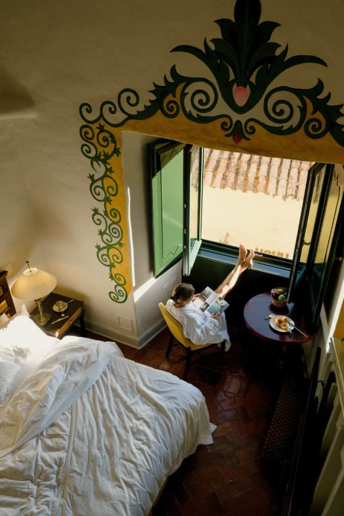 Woman reading a book and enjoying breakfast with her feet on the windowsill while sitting in a sunlit hotel room in Peru