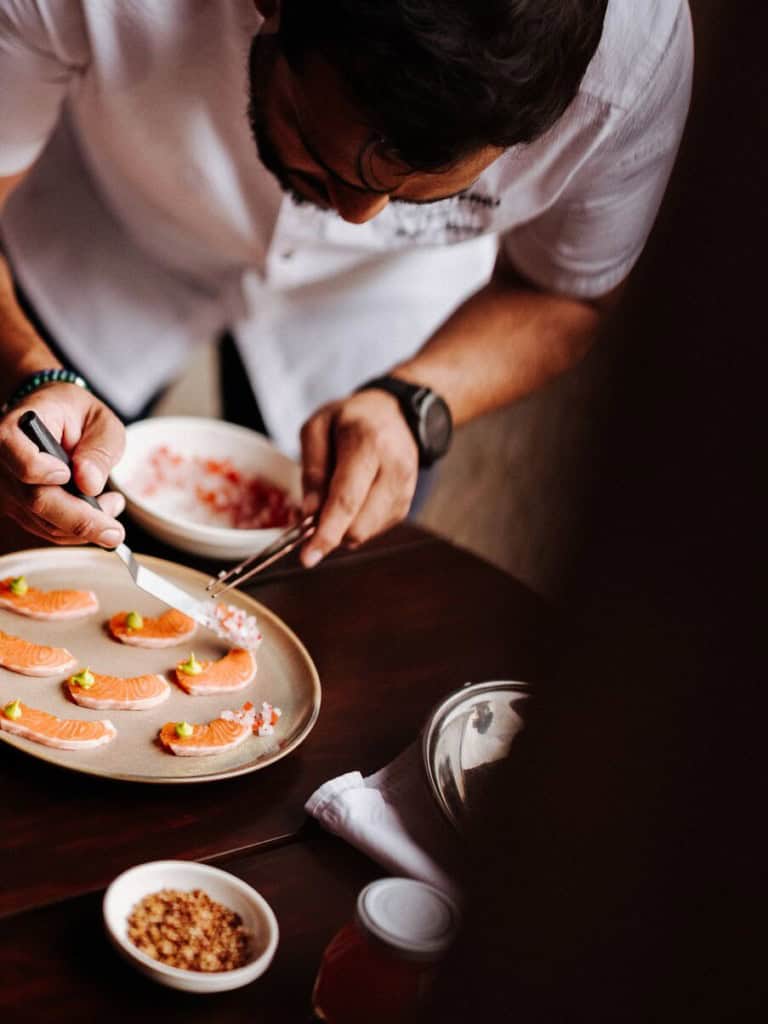 Chef carefully plating gourmet salmon slices with precision, adding fine garnishes in an upscale dining setting.